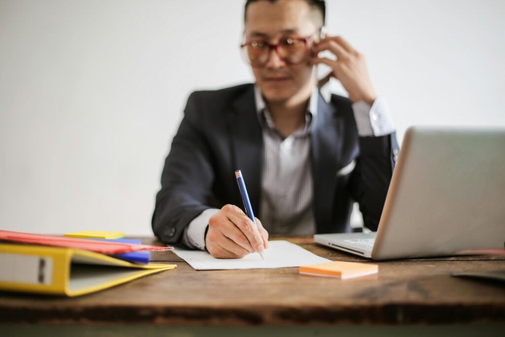 pexels photo 3760612 3760612 Businessman talking on phone while writing notes and using a laptop at desk.